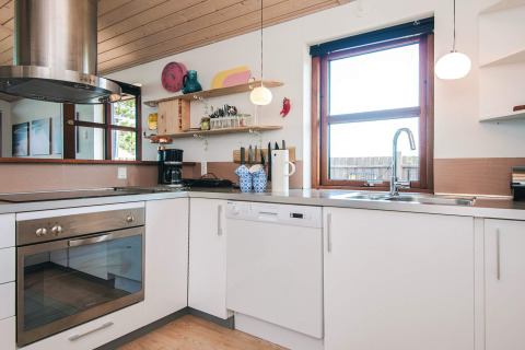 Modern kitchen at a 4 person holiday home in Glesborg, Denmark, with white cabinets, oven, and scenic window.