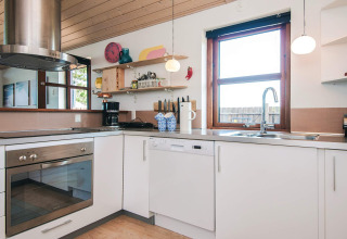 Cucina moderna in casa vacanze per 4 persone a Glesborg, Danimarca, con mobili bianchi e ampia finestra luminosa.