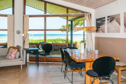 Salon et salle à manger avec grandes fenêtres et vue sur la mer dans une maison de vacances à Glesborg, Danemark.