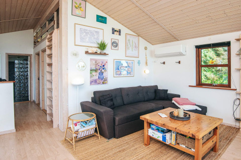 Hyggelig stue i feriebolig i Glesborg, Danmark, med mørkegrå sofa, træbord og vægkunst.