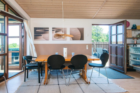 Essbereich im Ferienhaus in Glesborg, Dänemark, mit Holztisch, schwarzen Stühlen und Zugang zum Garten.