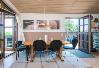 Sala da pranzo in una casa vacanze a Glesborg, Danimarca, con tavolo in legno, sedie nere e accesso al giardino.