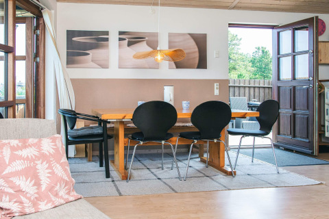 Eethoek van een vakantiehuis in Glesborg, Denemarken, met houten tafel, zwarte stoelen en open deur naar terras.