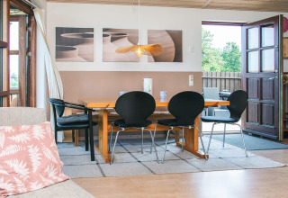 Spiseområde i et sommerhus i Glesborg, Danmark, med træbord, sorte stole og åbent dørområde til terrasse.