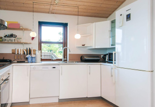 Cucina moderna con armadietti bianchi, grande finestra, elettrodomestici e soffitto in legno in una casa vacanze.