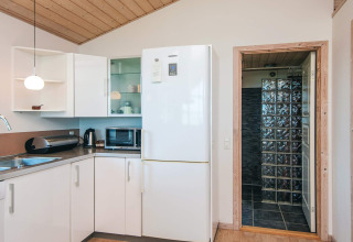Modern kitchen with white cabinets, large fridge, and doorway to bathroom in a Glesborg holiday home.