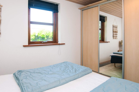 Dormitorio con cama doble, edredones azules, armario con espejo y ventana en casa de vacaciones en Glesborg, Dinamarca.