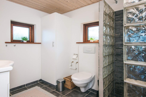 Moderne badeværelse med væghængt toilet, glasstensbruser og to små vinduer i et feriehus i Glesborg.