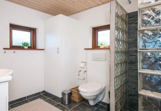 Modern bathroom with wall-mounted toilet, glass brick shower, and two small windows in a Glesborg lodge.