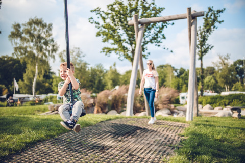 Een jongen lacht terwijl hij op een touwschommel zit in vakantiepark Ackersate, Gelderland, Nederland.