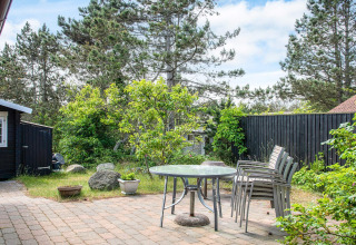 Gepflasterte Terrasse mit Glastisch und Stühlen, umgeben von Bäumen im Ferienhaus in Glesborg, Dänemark.