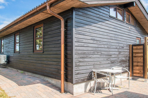Terrasse extérieure d'un lodge en bois noir avec table et chaises en métal, maison de vacances 4 personnes à Glesborg, Danemark.