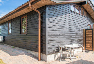 Terraza exterior de una cabaña de madera negra con mesa y sillas metálicas, casa de vacaciones para 4 en Glesborg, Dinamarca.