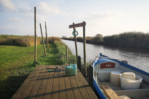 Pontons au bord d’un canal avec petite barque, matériel de pêche et verdure à Hemmet, Danemark.