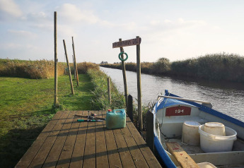 Pontons au bord d’un canal avec petite barque, matériel de pêche et verdure à Hemmet, Danemark.