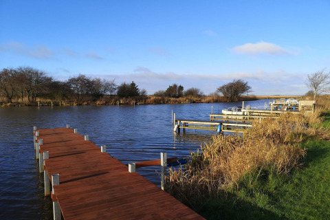 Holzsteg am Wasser mit Booten und Schilf beim 6-Personen-Ferienhaus in Hemmet, Dänemark an einem klaren Tag.