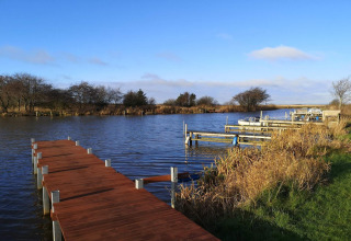Muelle de madera junto al agua con botes y juncos cerca de la casa de vacaciones en Hemmet, Dinamarca.