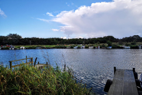 Blick auf einen ruhigen Fluss mit Booten, Stegen und Schilf am 6-Personen-Ferienhaus in Hemmet, Dänemark.