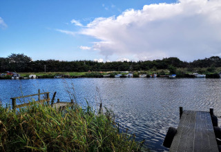 Uitzicht op een rustige rivier met boten, steigers en riet bij het 6-persoons vakantiehuis in Hemmet, Denemarken.