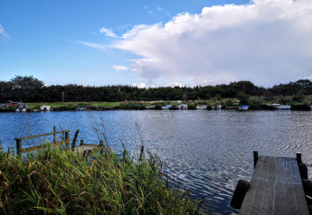 Uitzicht over een rustige rivier met boten, steigers en riet bij het 6-persoons vakantiehuis in Hemmet, Denemarken.