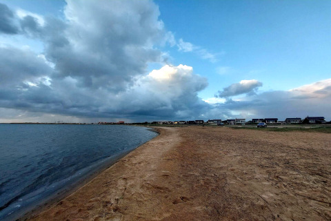 Skyet himmel over strand og hytter ved '6 personers feriehus i Hemmet', Danmark, tæt på vandet.