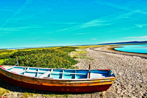 Une vieille barque repose sur la rive sablonneuse d'une rivière près de Hemmet, Danemark, sous un ciel bleu.
