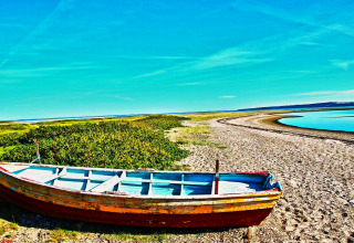 En gammel båd står på en strand ved en flod med blå himmel i nærheden af Hemmet, Danmark.