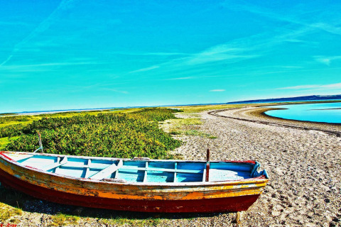 En gammel båd står på en strand ved en flod med blå himmel i nærheden af Hemmet, Danmark.