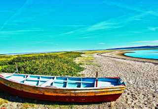 En gammel båd står på en strand ved en flod med blå himmel i nærheden af Hemmet, Danmark.