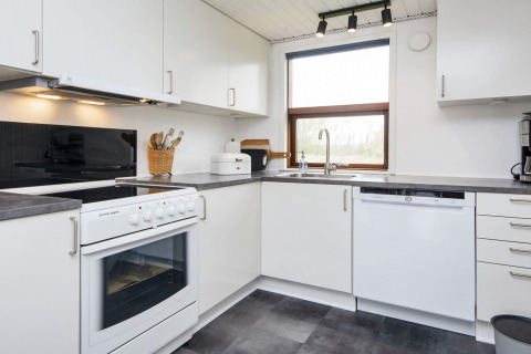 Cuisine blanche moderne dans maison de vacances à Hemmet, Danemark, avec four, lave-vaisselle et grande fenêtre.