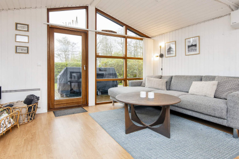 Moderne woonkamer van een vakantiehuis in Hemmet, Denemarken, met grote ramen, zetel en houten tafel.