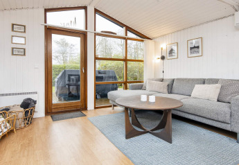 Moderne woonkamer in een vakantiehuis in Hemmet, Denemarken, met grote ramen, grijze bank en tafel.