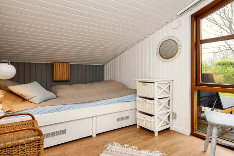 Chambre douillette avec plafond incliné, lit simple, commode blanche et vue sur le jardin par une grande fenêtre.