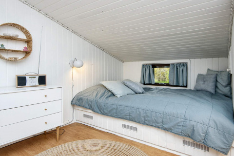 Camera accogliente in una lodge danese con soffitto inclinato, pareti bianche, letto blu e piccola finestra.