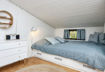 Chambre confortable dans un lodge danois, plafond incliné, murs blancs, literie bleue et petite fenêtre.