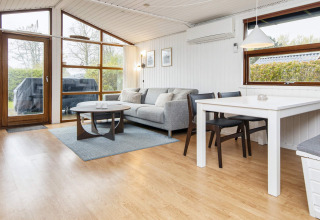 Salon moderne avec canapé gris, table à manger et grandes fenêtres dans un gîte à Hemmet, Danemark.