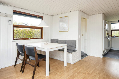 Coin repas lumineux dans une maison de vacances à Hemmet, Danemark, table, banc et vue sur la cuisine.
