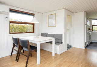 Lyst spisekøkken i feriehytte i Hemmet, Danmark, med spisebord, bænk og køkken i baggrunden.
