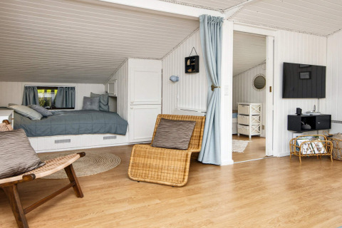 Espace séjour lumineux dans maison de vacances à Hemmet, Danemark, avec lit, fauteuils et TV.