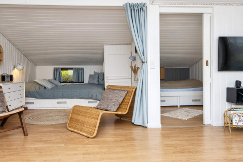 Gezellige woonkamer met twee nisbedden, blauwe gordijnen en houten vloer in vakantiehuis Hemmet, Denemarken.