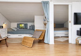 Zona giorno accogliente con due letti in nicchia, tende blu e pavimento in legno in una casa vacanza a Hemmet.