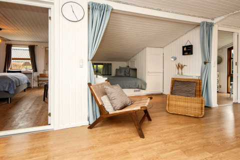 Salon avec murs en bois blanc et accès aux chambres dans une maison de vacances à Hemmet, Danemark.