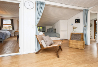 Stue med hvide træpaneler og åbne døre til soveværelser i et feriehus i Hemmet, Danmark.