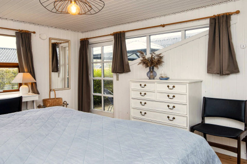 Chambre dans une maison de vacances à Hemmet, Danemark, avec lit, commode et grandes fenêtres rideaux.