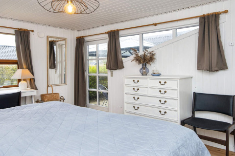 Slaapkamer in een vakantieverblijf in Hemmet, Denemarken, met bed, wit ladenkastje en grote ramen.