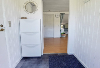 Entrée d'une maison de vacances à Hemmet, Danemark, avec murs blancs, armoire à chaussures et miroir rond.