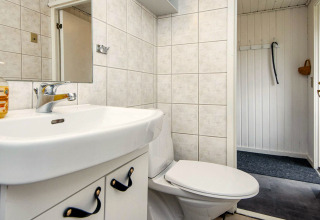Salle de bain dans une maison de vacances à Hemmet, Danemark, avec carrelage blanc, WC, lavabo et miroir.