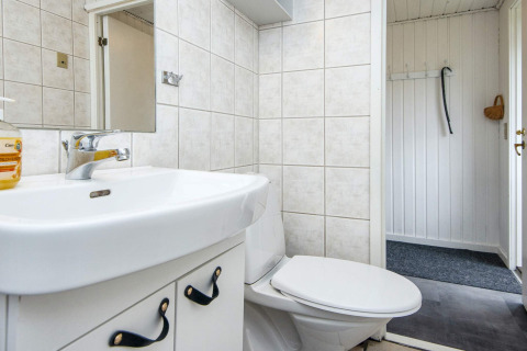 Badezimmer in einer Ferienunterkunft mit weißen Fliesen, WC, Waschbecken und Spiegel in Hemmet, Dänemark.