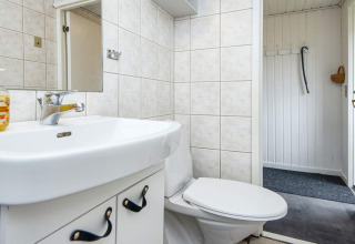 Badkamer in een vakantiehuis met witte tegels, toilet, lavabo en spiegel, gelegen in Hemmet, Denemarken.