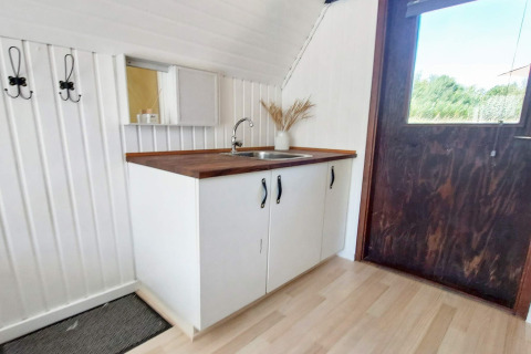 Kleine keukenhoek met houten werkblad, spoelbak en witte kasten in een vakantiehuis in Hemmet, Denemarken.